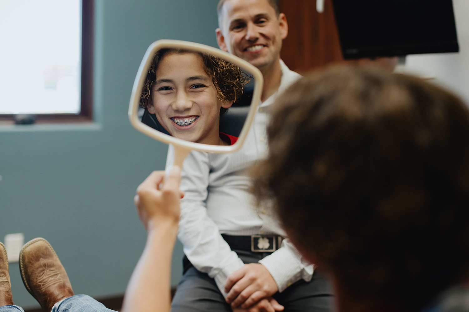 Dr. David Gallup smiling at a young male patient who is looking at himself in the mirror